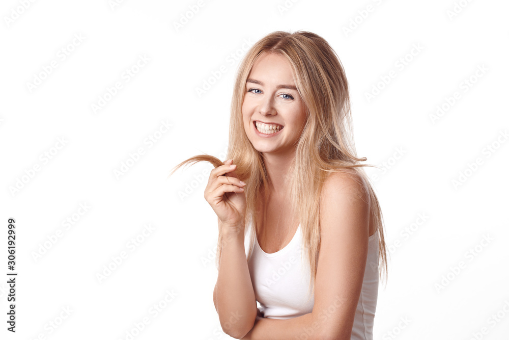 Attractive young blond woman with a friendly happy smile grinning at the camera as she plays with a strand of her long hair isolated on white Attractive young blond woman with a friendly happy smile grinning at the camera as she plays with a strand of her long hair isolated on white