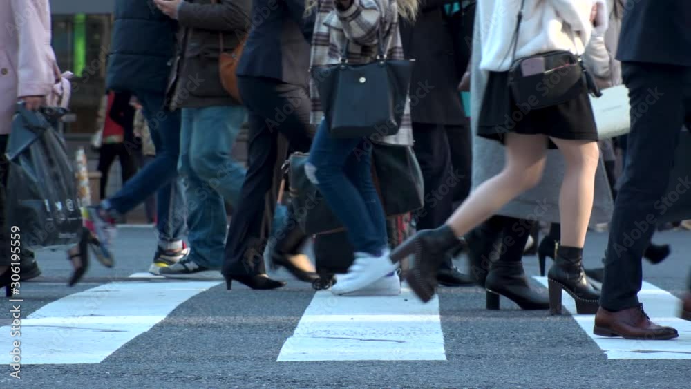 TOKYO, JAPAN - NOV 2019 : Crowd of people at Shibuya Scramble Crossing in busy early evening rush hour. Many commuters and tourists at the street. Shot in sunset time. In front focus. Slow motion. TOKYO, JAPAN - NOV 2019 : Crowd of people at Shibuya Scramble Crossing in busy early evening rush hour. Many commuters and tourists at the street. Shot in sunset time. In front focus. Slow motion.