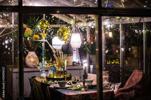 Decorated greenhouse in trendy christmas setting with dinner table, candles and christmas lights.
