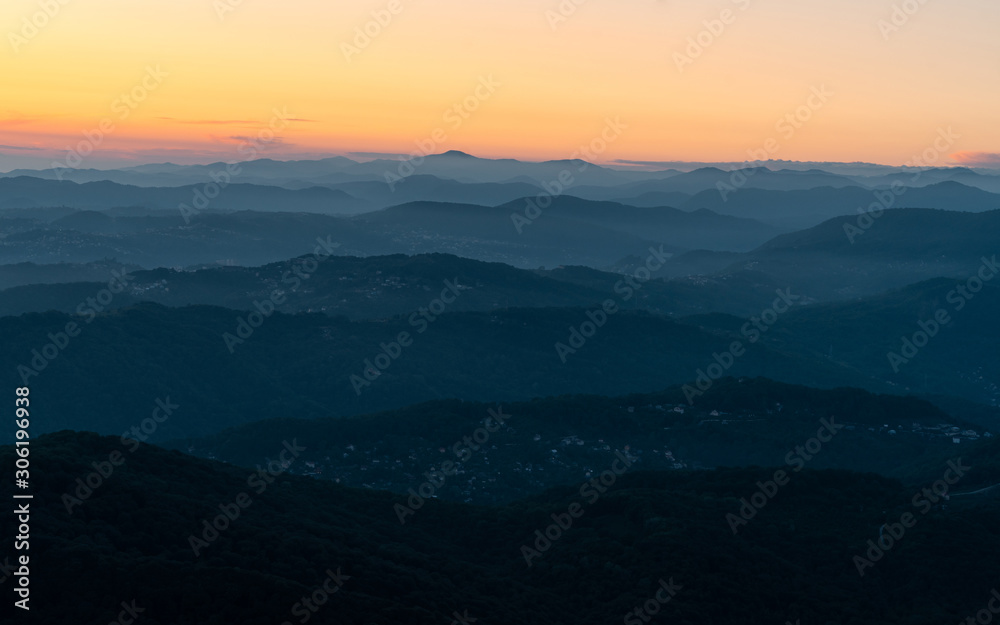 Panorama of a mountain landscape at sunset. Hills blue gradient background. Orange sky on the horizon. Misty evening in the mountains.
