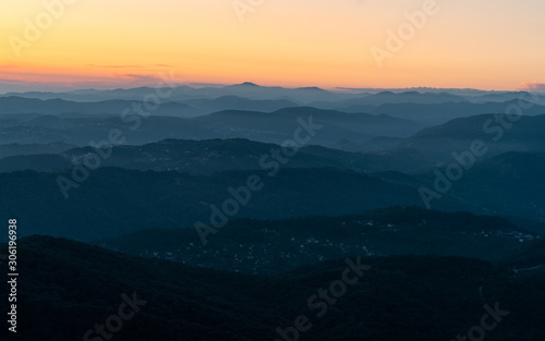 Panorama of a mountain landscape at sunset. Hills blue gradient background. Orange sky on the horizon. Misty evening in the mountains.