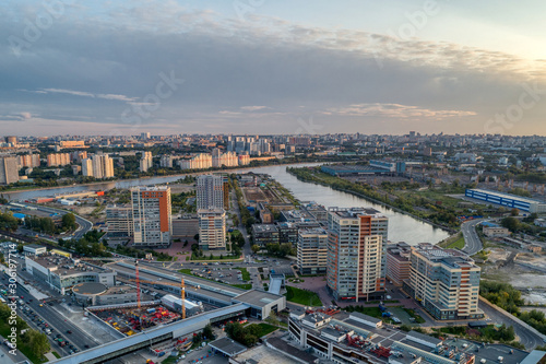 Big city aerial shot. Long and wide streets filled with cars. Dense forest vegetation on the banks of the river. Shooting in the evening with the setting sun.