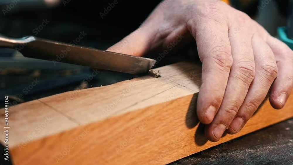Carpentry industry - a man woodworker cutting out and smoothing the recess on the wooden detail with a chisel