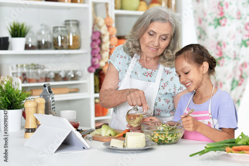 Portrait of cute little girl with her grandmother cooking together at kitchen table