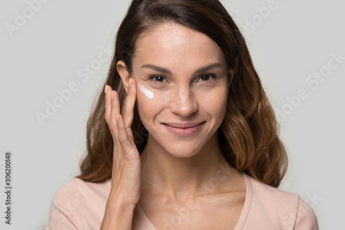 Head shot portrait beautiful young woman applying cosmetic cream