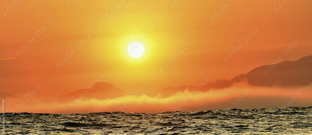 Seascape.  Red dawn sky,  Morning fog over the ocean, silhouettes of mountains on the horizon.  South Africa.