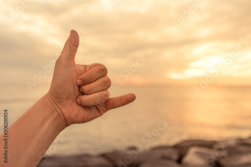 Hand showing shaka hang loose sign on ocean background. 