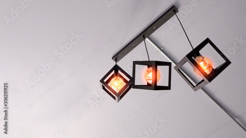 Low angle view of modern three metal cage hanging lamps with electrical conduit pipe on white ceiling inside incomplete room, renovation and home interior concept