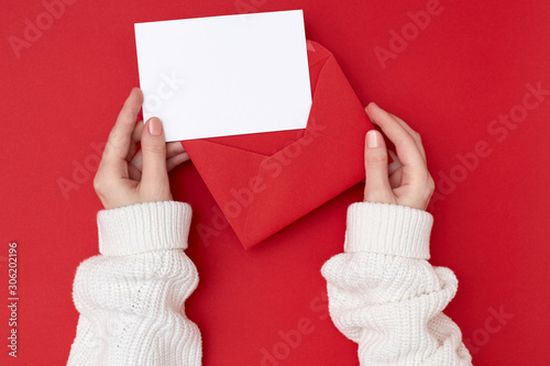 Women's hands holding an empty postcard and red envelope on the red background. Christmas concept