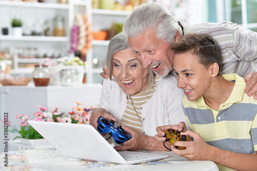 Portrait of happy senior couple with grandson using laptop playing game