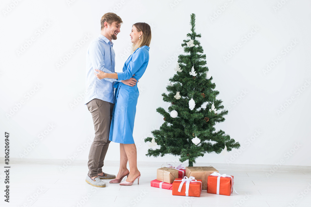 Holidays and festive concept - Young happy couple near a Christmas tree on white background