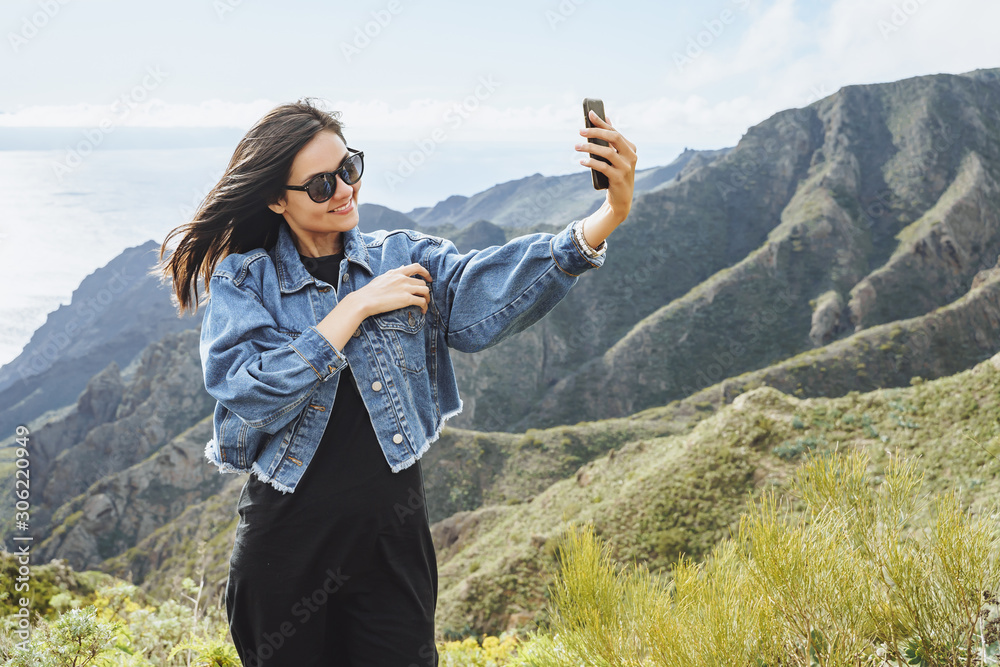 Happy woman tourist taking selfie using smartphone on top of a mountain