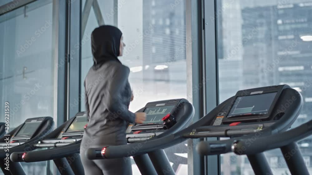 Athletic Muslim Sports Woman Wearing Hijab and Sportswear Running on a Treadmill. Energetic Fit Female Athlete Training in the Gym. Female Only Fitness Club for Workout and Training. Back View 