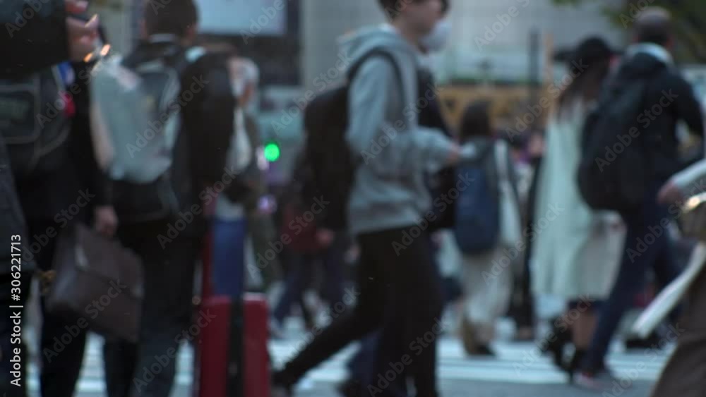 TOKYO, JAPAN - NOV 2019 : Crowd of people at Shibuya Scramble Crossing in busy early evening rush hour. Many commuters and tourists at the street. Shot in sunset time. In front focus. Slow motion.