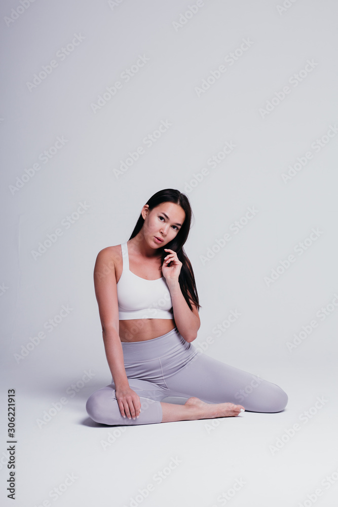Fototapeta premium Athletic young woman doing yoga on a white background - the concept of a healthy lifestyle and a natural balance between the body and mental development, in gray leggins and white T-shirt