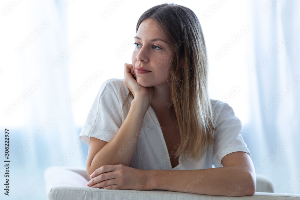 Pretty young woman looking to sideways while sitting on sofa at home. Pretty young woman looking to sideways while sitting on sofa at home.