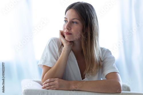 Pretty young woman looking to sideways while sitting on sofa at home.