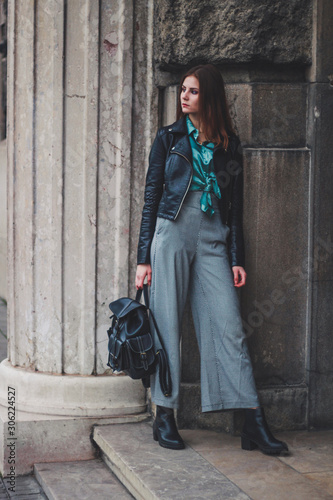 Fashion shooting. Wide trousers tube. Satin emerald blouse. Fashion trend. Tall brunette model. Black eco leather jacket.Stylish backpack made of eco leather. Handbag. © Yaroslav