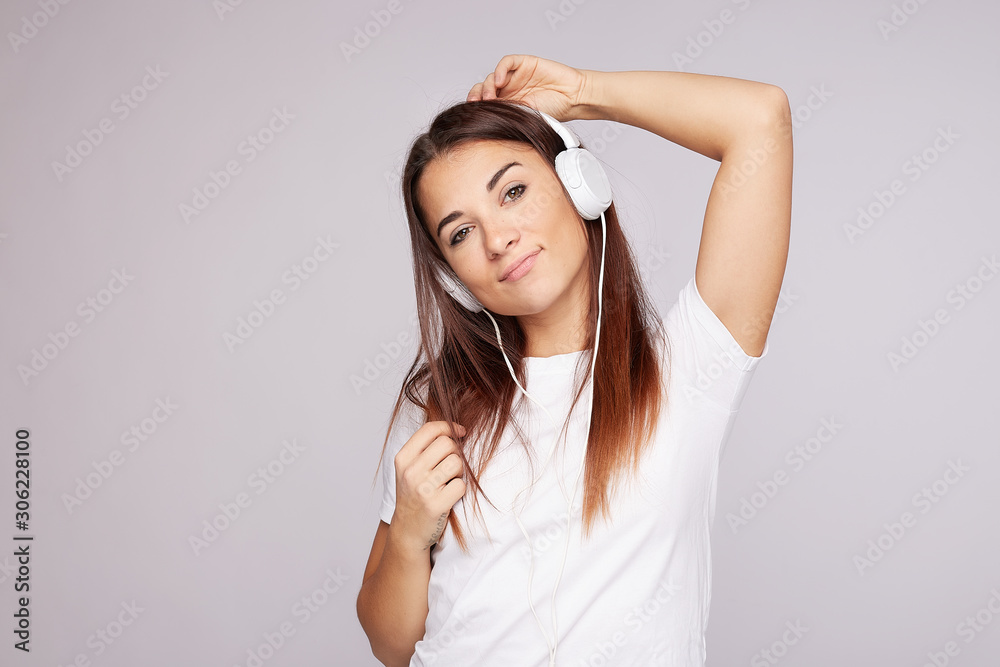 Happy young mixed raced tan skinned lady enjoys every bit of pleasant melody, dances and gestures actively, wears stereo headphones, looks at camera, wears casual black t shirt, isolated on grey wall Happy young mixed raced tan skinned lady enjoys every bit of pleasant melody, dances and gestures actively, wears stereo headphones, looks at camera, wears casual black t shirt, isolated on grey wall