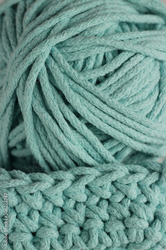 Knitting and hand crochet concept. A fragment of a knitted product and a ball of cord close up. Tiffany color yarn background.