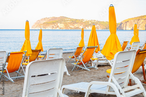 White plastic and metal construction with yellow fabric deckchairs together with yellow umbrellas on the sand beach of Tyrrhenian sea with mountains on background in Italy photo