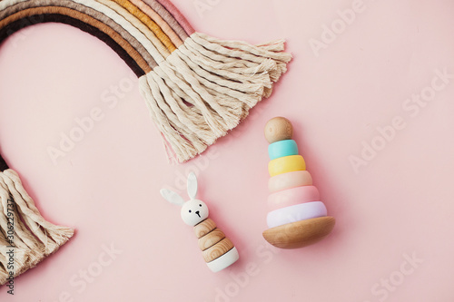  Eco friendly plastic free toys for toddler. Stylish wooden toys for child on pink background. Modern colorful wooden pyramid with rings, wooden bunny and macrame rainbow.