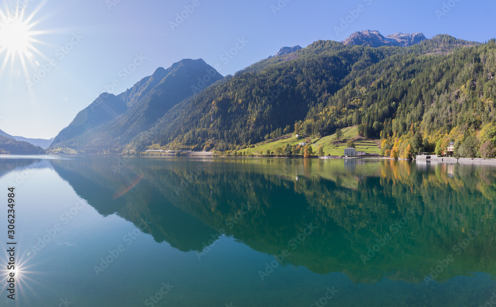 Reflection of sun, mountains and forest in barrier lake of Poschiavo, Graubünden Switzerland