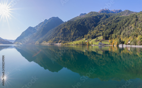 Reflection of sun  mountains and forest in barrier lake of Poschiavo  Graub  nden Switzerland