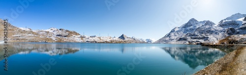 Panoramic view of Lago Bianco at Bernina pass. Lake reflects mountain range covered in snow and the blue sky. Picture taken after midday in late Septemeber © str0pe photography
