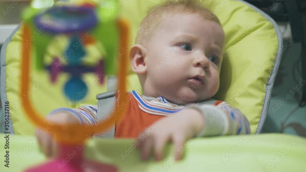 funny little boy tries to take bright plastic toy from table sitting in soft green highchair at home extreme close view funny little boy tries to take bright plastic toy from table sitting in soft green highchair at home extreme close view