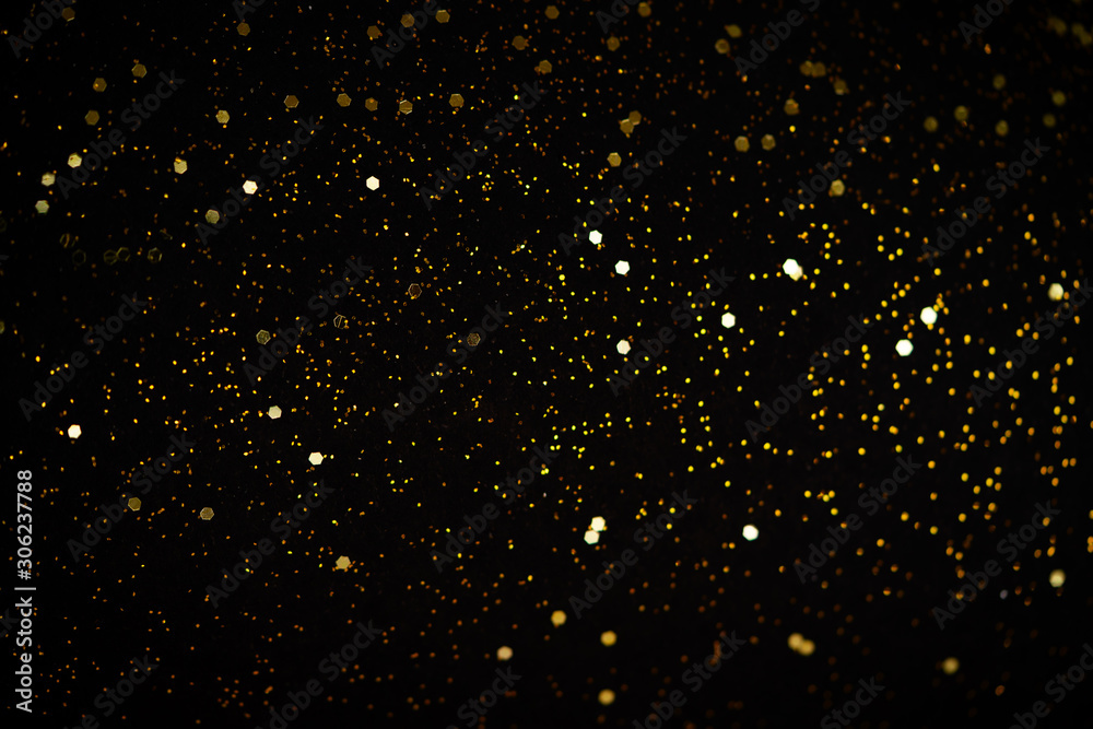 Beautiful Christmas light background. Abstract glitter bokeh and scattered sparkles in gold, on black
