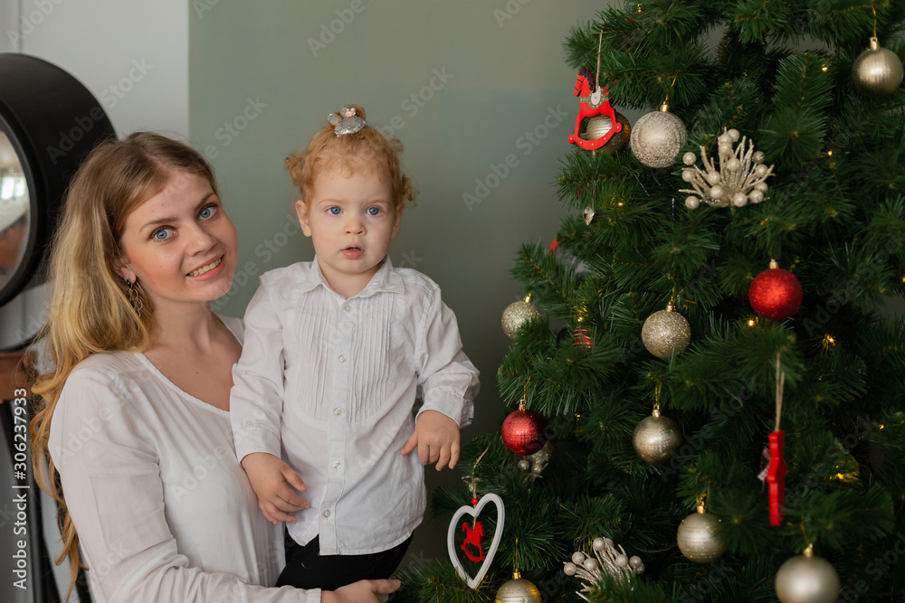 Beautiful happy mother with a daughter in her arms at the Christmas tree. Merry Christmas 2020. Beautiful happy mother with a daughter in her arms at the Christmas tree. Merry Christmas 2020.