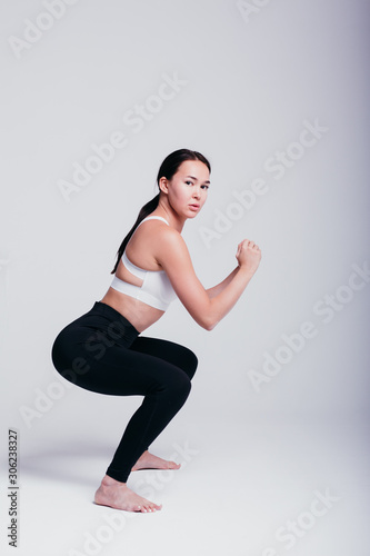 girl shows poses for yoga and warm-up in black leggings and a white T-shirt barefoot on a white background