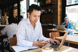 Hardworking ethnic businessman using gadgets in coffee shop