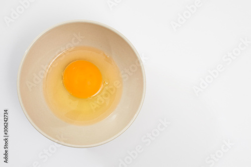 Broken egg in a beige bowl on white background