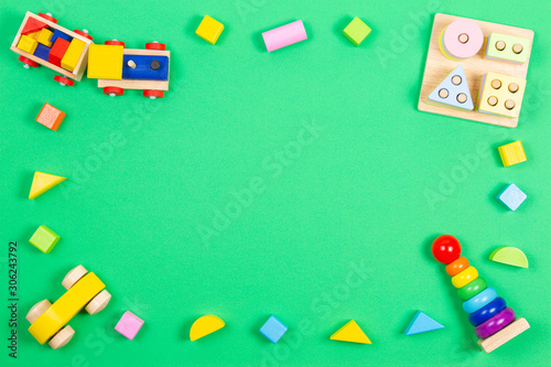 Baby kids toys background. Wooden educational geometric stacking blocks toy, wooden train, car, red airplane and colorful blocks on green background. Top view, flat lay