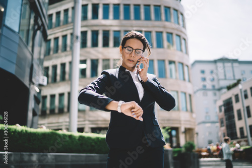 Attractive confident female boss calling to employee for clarify time of meeting in business district, serious woman dressed in formal suit making important intern?tional call via app on cellular photo