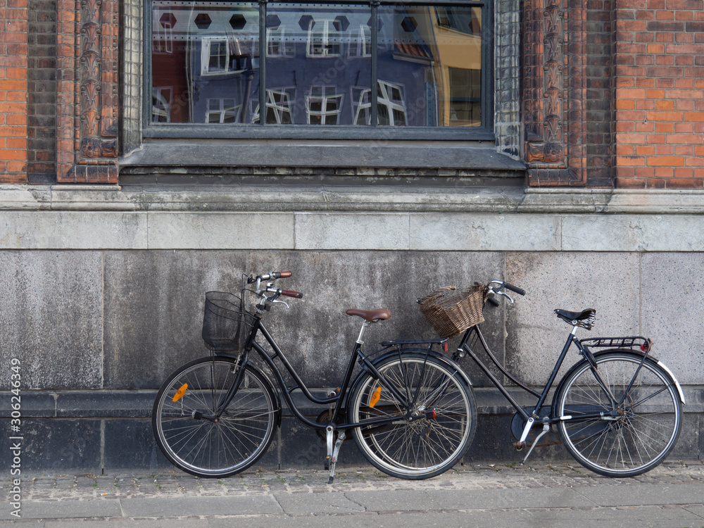 Two bikes at rest on concrete and brick wall with window in Copenhagen