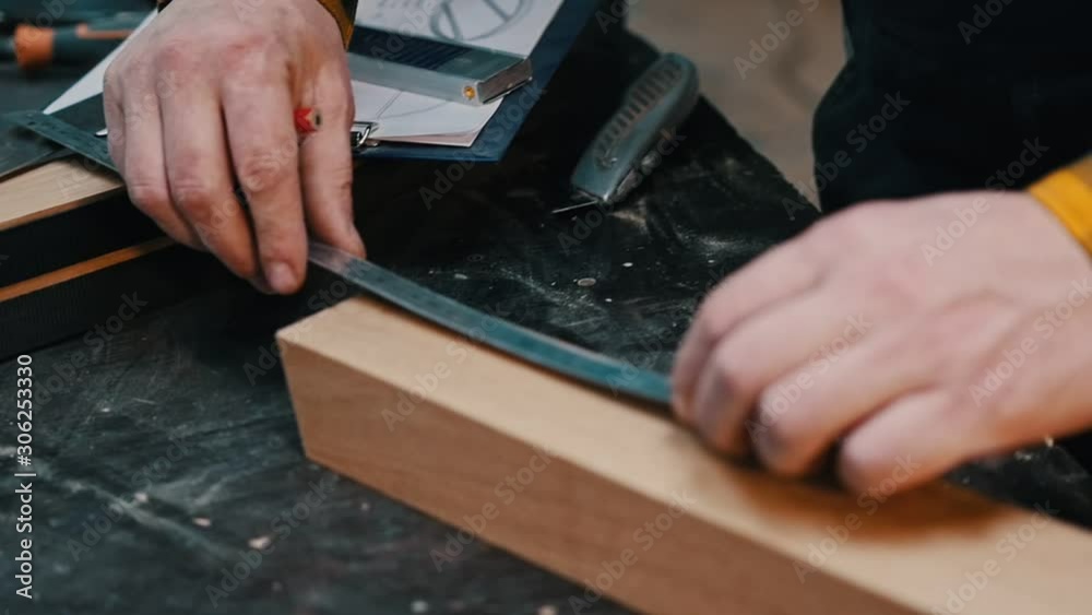 Carpentry indoors - a woodworker measuring the wooden piece with a yardstick Carpentry indoors - a woodworker measuring the wooden piece with a yardstick