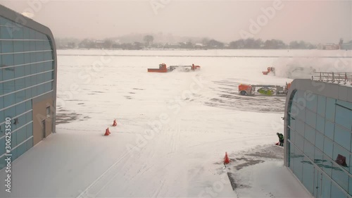 Lviv, Ukraine - January, 2019: Orange snowplows clean the runway and the apron of the airfield. Snowfall and heavy snowstorm. Weather anomaly flight delay concept.