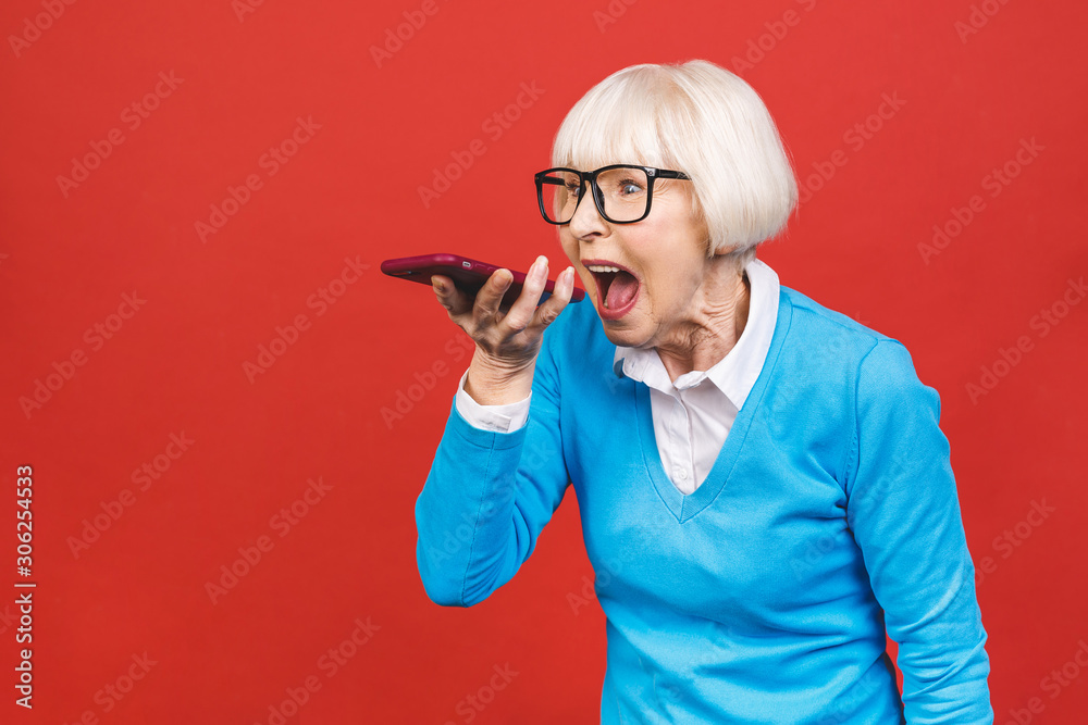 Angry senior woman talking phone isolated on red background. Angry senior woman talking phone isolated on red background.