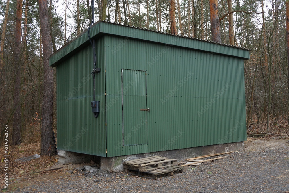 a large iron green trailer with a door stands among pine trees in a park a large iron green trailer with a door stands among pine trees in a park