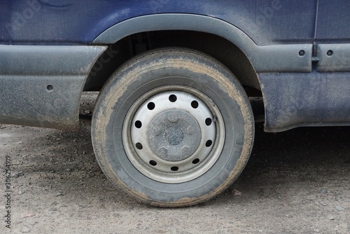 one gray dirty wheel on a blue car stands on the asphalt of the road