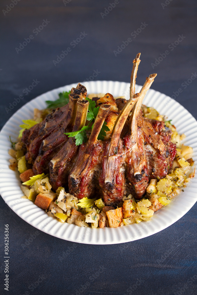 Crown roast of pork stuffed with apples and bread crumbs and celery sticks on white plate