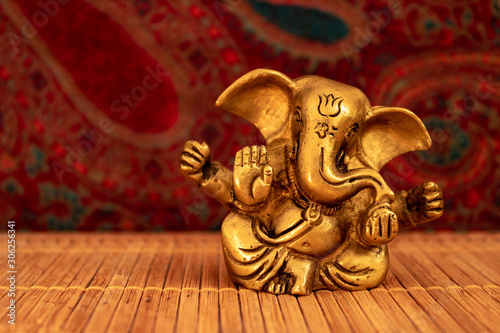 Golden Ganesha statue on bamboo mat and oriental background, close up