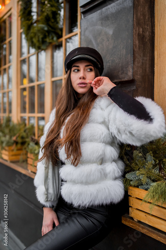 Obraz na płótnie Beautiful young caucasian woman wearing natural short white fur coat posing for a portrait near Christmas showcase. Christmas decor. Fashion. Style. Winter clothes made of natural fur. Vertical w salonie