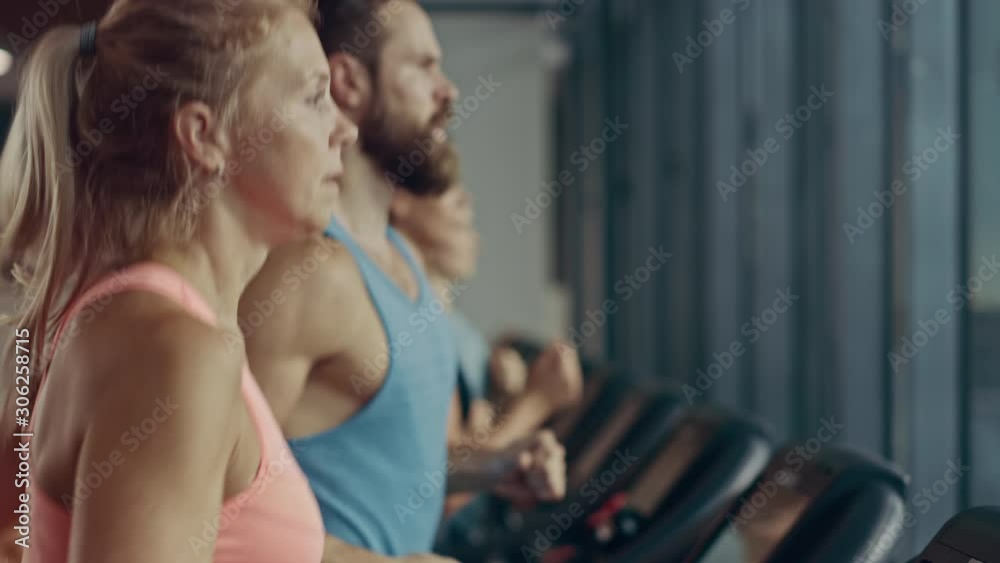 Fit Athletic Woman Running on the Treadmill, Doing Her Fitness Exercise. Muscular Women and Men Actively Training in the Modern Gym. Sports People Workout in Fitness Club. Side View Slow Motion Fit Athletic Woman Running on the Treadmill, Doing Her Fitness Exercise. Muscular Women and Men Actively Training in the Modern Gym. Sports People Workout in Fitness Club. Side View Slow Motion