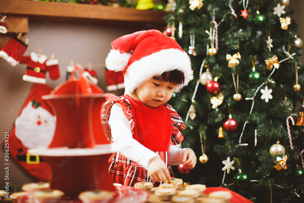 toddler girl helping preparing mice pie for Christmas party in front of Christmas tree toddler girl helping preparing mice pie for Christmas party in front of Christmas tree