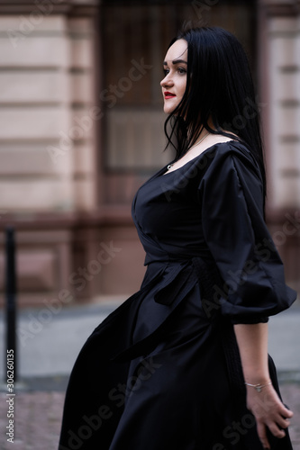 Autumn fashion outdoor. The girl with red lips in fashionable stylish black dress, autumnal lifestyle on the background of blurry yellow-green trees in the park. Vertical