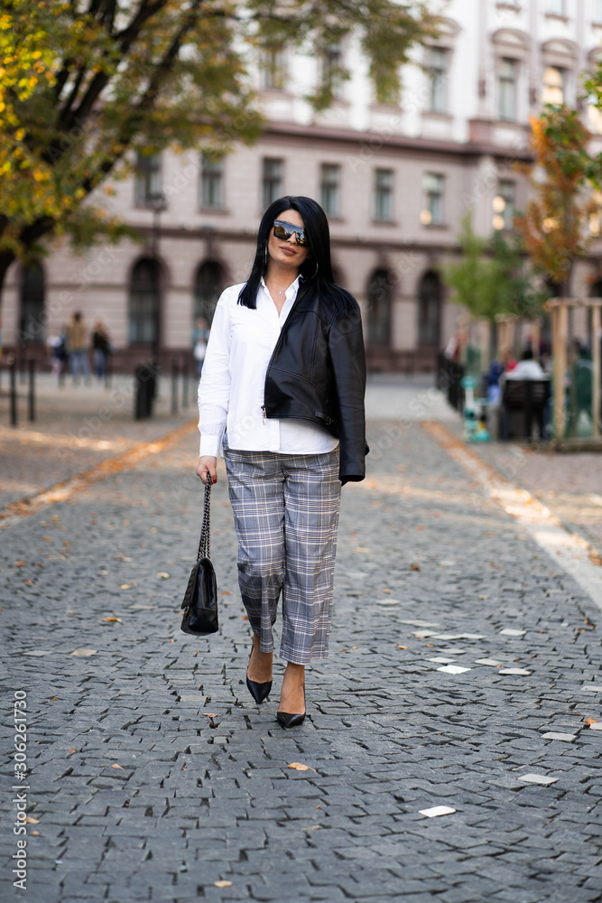 Autumn fashion outdoor. The girl in fashionable stylish white shirt , pants, jacket and sunglasses, autumnal lifestyle on the background of blurry yellow-green trees in the park. Vertical Autumn fashion outdoor. The girl in fashionable stylish white shirt , pants, jacket and sunglasses, autumnal lifestyle on the background of blurry yellow-green trees in the park. Vertical